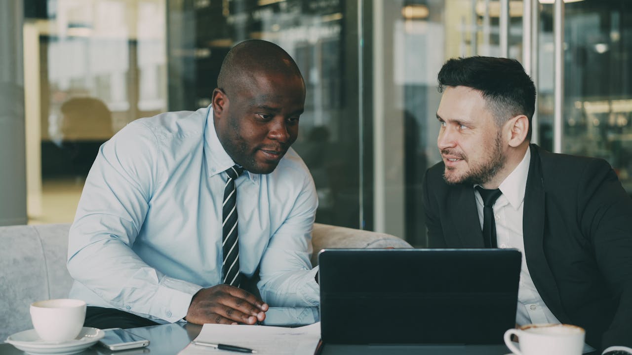 Two businessmen collaborating in an office setting, discussing ideas over a laptop.