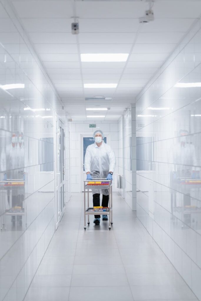 Scientist in protective clothing walking with cart in a sterile laboratory corridor.