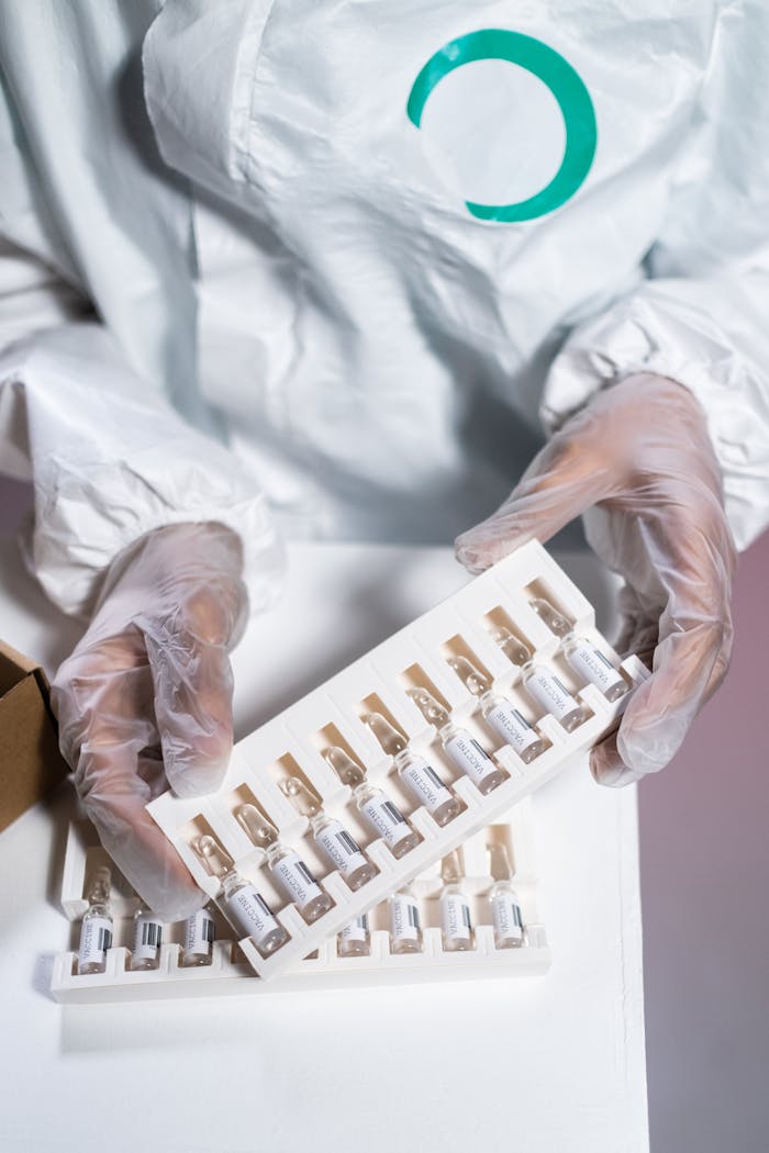 Healthcare worker in protective gear handling vials in a laboratory setting.